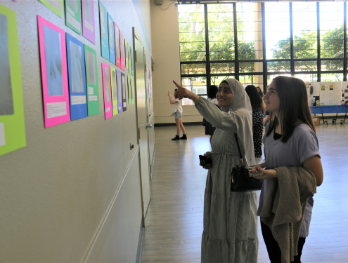 Two young students point at a piece of student artwork on the wall in neon colors.