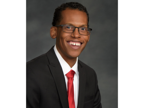 Board Member Terrence Shelton, in a black jacket, white shirt, and red tie smiles, poses for a portrait photo.